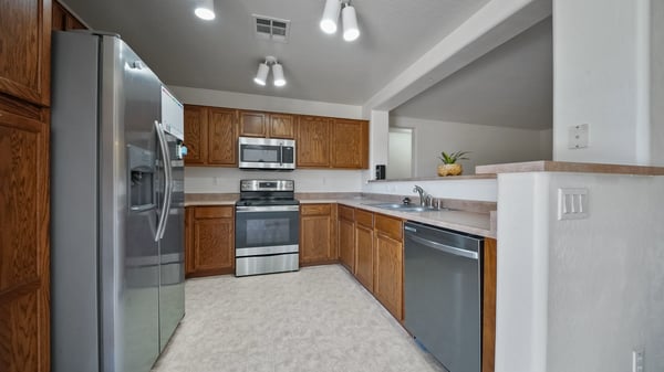 Functional kitchen includes abundant cabinetry, stainless steel appliances, generous counter space, and a breakfast bar that opens to the living area, creating a practical layout for cooking and entertaining.