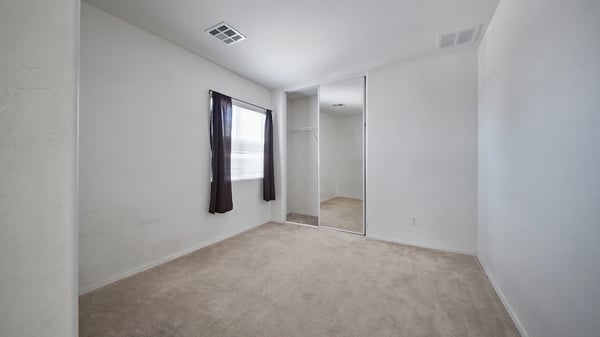 Bright secondary bedroom features plush carpeting, mirrored closet doors, and plenty of natural light. Ideal for guests, family, or a dedicated home office in this Buckeye property.