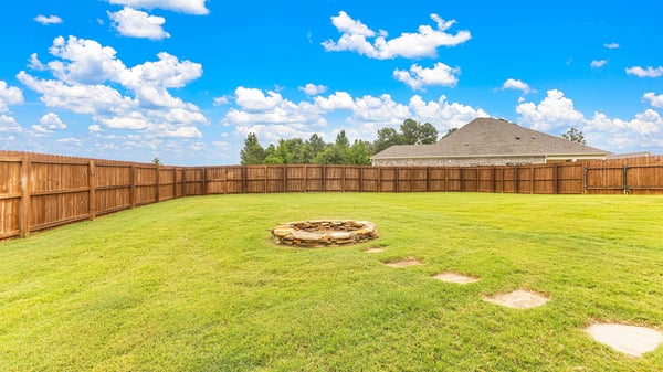 Spacious backyard featuring a stone fire pit and a privacy fence, perfect for outdoor gatherings.