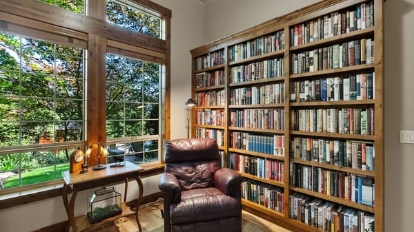 Bright reading nook featuring a cozy chair, built-in bookshelf, and large windows with garden views.