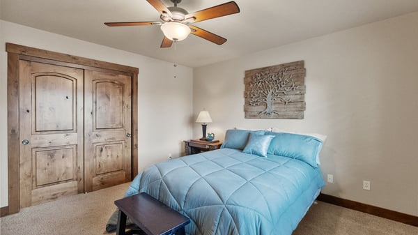 Cozy bedroom featuring a ceiling fan, natural wood accents, and ample storage with double doors.