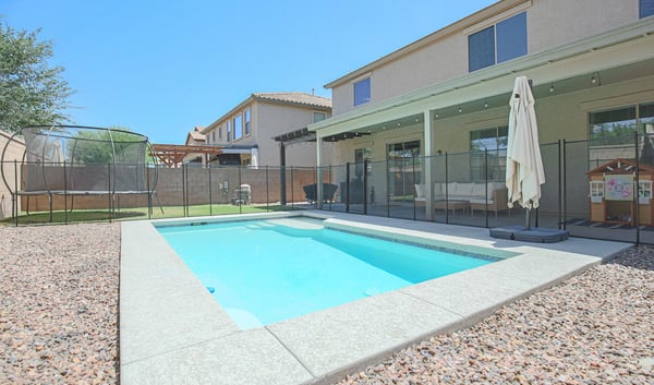 Private backyard featuring a sparkling pool, covered patio, removable pool fence, and lush lawn. A fantastic outdoor space for entertaining, relaxing, and enjoying Arizona's sunny climate.