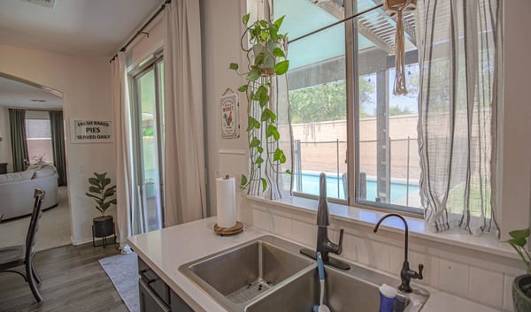 Functional kitchen workspace with a modern sink, quartz countertops, updated fixtures, and relaxing views of the covered patio and sparkling backyard pool, blending style with everyday convenience.