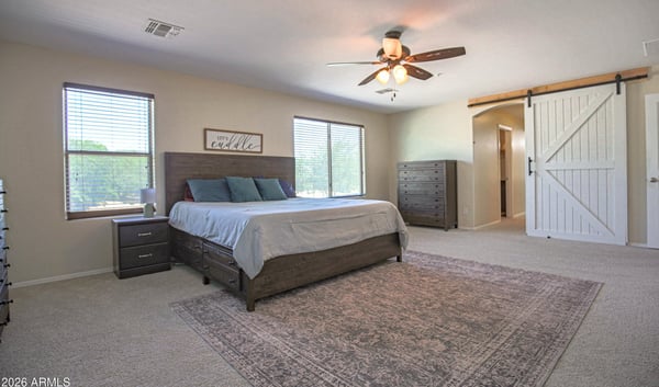 Oversized owner's suite featuring plush carpeting, abundant natural light, ceiling fan, and sliding barn door access to the private en-suite bath. A peaceful retreat in this desirable Waddell home.