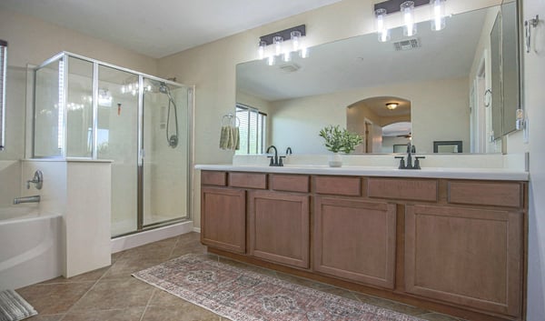 Elegant primary bathroom with an extended dual-sink vanity, oversized mirror, updated lighting, soaking tub, and separate glass shower. A spacious and functional owner's retreat.