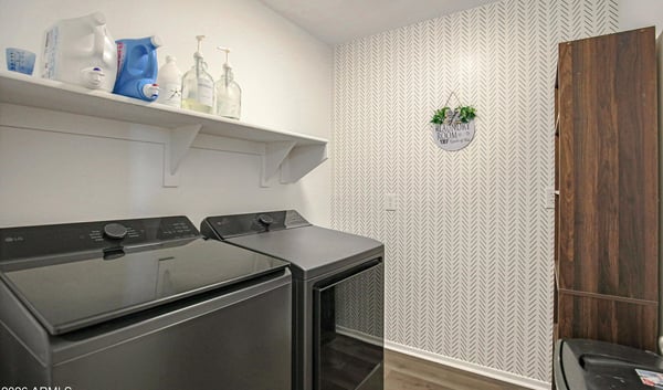 Well-appointed laundry room featuring stylish wallpaper, modern flooring, upper shelving, and dedicated space for laundry appliances. A practical upgrade for everyday living in this Waddell home.