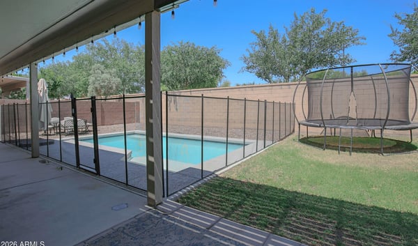 Covered patio overlooking the backyard pool, grassy area, and secure pool fencing, creating a comfortable outdoor retreat for relaxing and entertaining in this Waddell home.