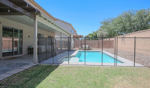 Spacious backyard featuring a fenced pool, covered patio, and open green space ideal for recreation and outdoor enjoyment. A well-designed backyard retreat in desirable Waddell.