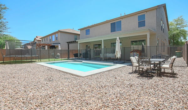 Wide backyard view highlighting the sparkling pool, covered patio, outdoor dining area, and generous outdoor space. A perfect setting for entertaining and enjoying life in Waddell.