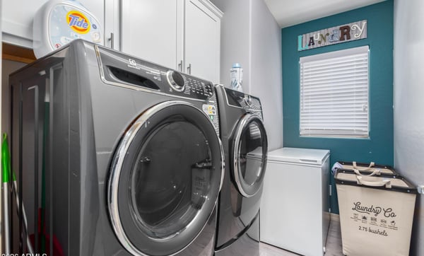 This dedicated laundry room features upper cabinetry for storage, modern laundry appliances, and a window providing natural light. A practical and organized utility space enhances everyday convenience.