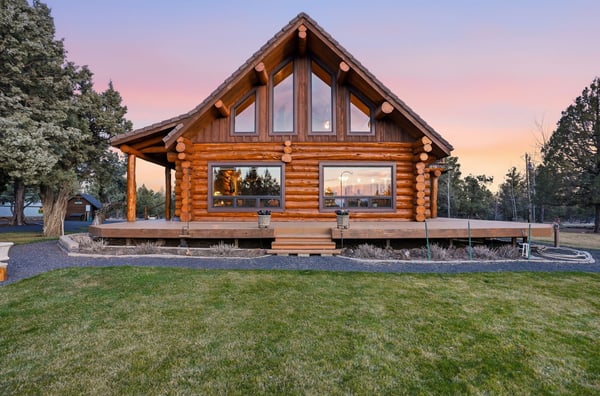 Stunning log cabin with expansive windows, surrounded by picturesque landscapes and vibrant sunset views.