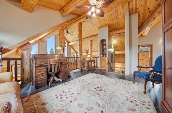 Spacious loft area with rustic wooden beams, featuring a cozy workspace and scenic views of nature.