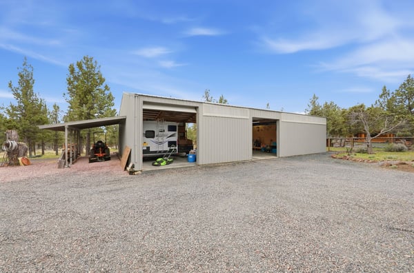 Spacious metal garage with ample parking and storage options, surrounded by open land and natural scenery.