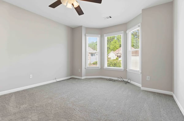 Bright and airy bedroom featuring large windows, plush carpeting, and a ceiling fan for comfort.