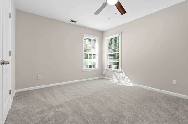 Bright and spacious bedroom featuring ample natural light, new carpeting, and modern ceiling fan for comfort.