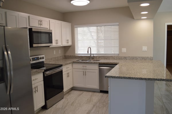 Updated kitchen featuring granite countertops, stainless steel appliances, white cabinets, and modern fixtures. Bright finishes and functional design make this kitchen a standout feature of the Phoenix home.