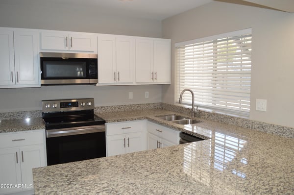 Modern kitchen showcasing granite countertops, stainless steel appliances, white shaker cabinets, and generous counter space. Natural light and thoughtful updates create a bright, welcoming atmosphere.