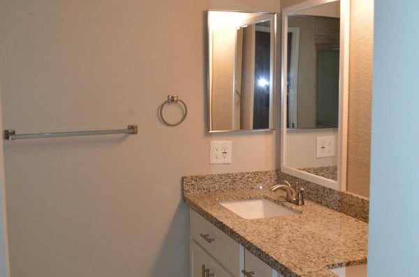 Renovated bathroom featuring dual sinks, granite countertops, white shaker cabinetry, updated lighting, and modern fixtures. A bright and functional space with quality finishes throughout.