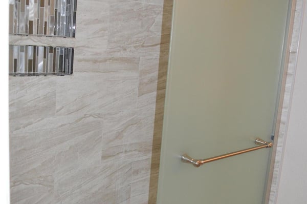 Modern glass-enclosed shower with custom tile walls and decorative insets creates a spa-like atmosphere. Stylish upgrades elevate the appeal of this beautifully renovated Phoenix home.