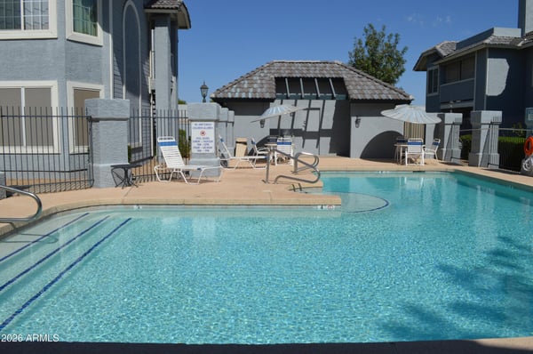 Resort-style swimming pool with sparkling water, poolside seating, shaded umbrellas, and a nearby clubhouse area. Enjoy outstanding community amenities in this desirable Phoenix location.