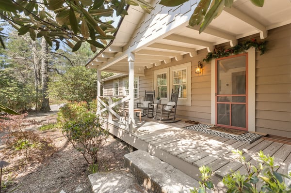 This inviting home features a spacious front porch surrounded by lush greenery, perfect for outdoor relaxation.