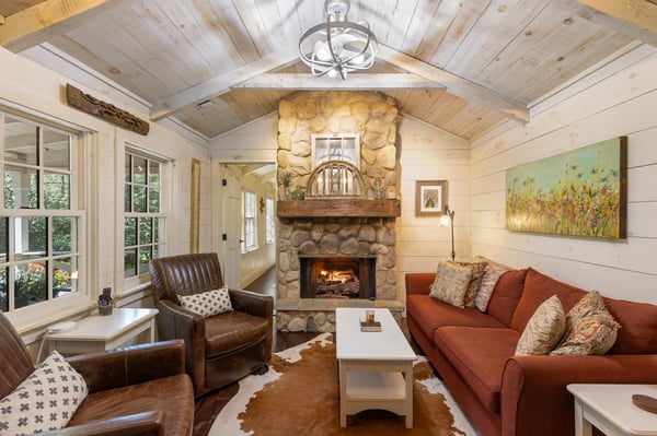 Cozy living area featuring a stone fireplace, rustic beams, and inviting natural light throughout.