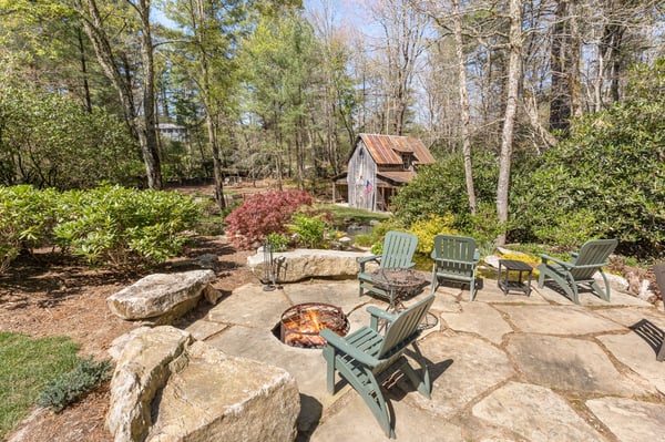 This inviting outdoor space features a fire pit surrounded by natural stone and lush landscaping, perfect for gatherings.
