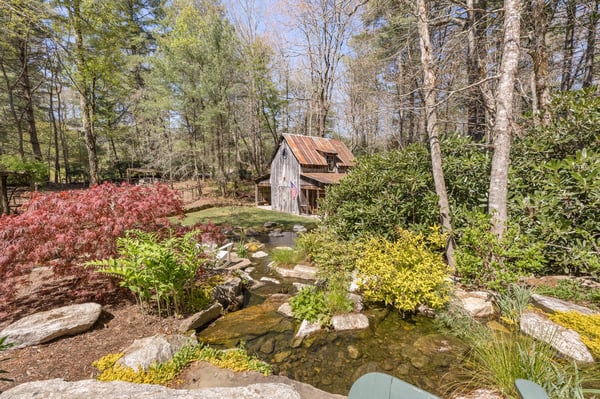 Discover a secluded retreat featuring a tranquil pond, vibrant landscaping, and a rustic cabin nestled among the trees.