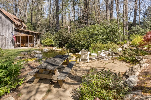 Discover a peaceful outdoor space featuring a rustic cabin, pond, and inviting seating area amid lush greenery.