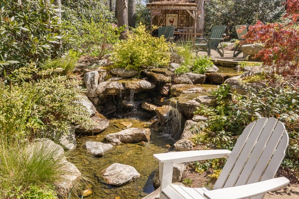 A tranquil outdoor retreat featuring a flowing stream, lush greenery, and inviting seating areas for relaxation.