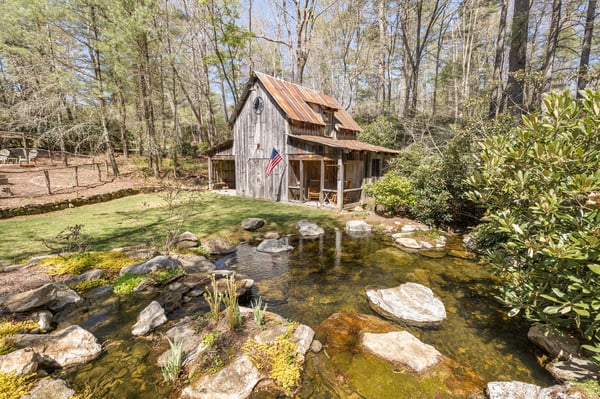 Secluded rustic cabin by a tranquil pond, surrounded by lush greenery and natural rock formations.