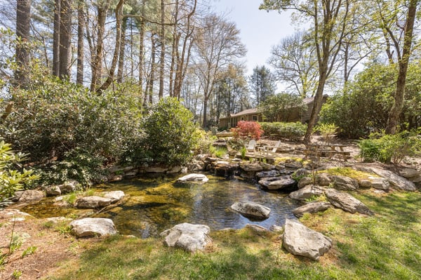 Secluded backyard oasis featuring a tranquil pond surrounded by lush greenery and natural stone accents.