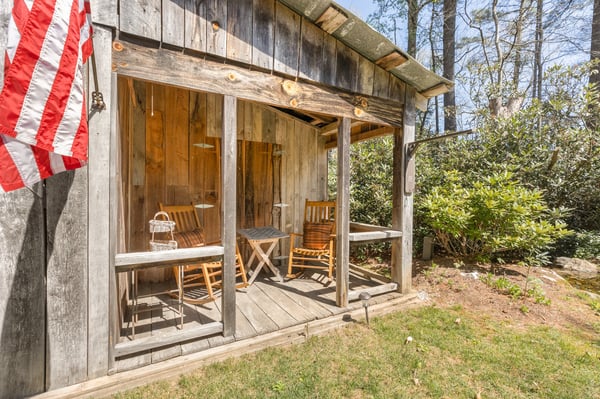 A rustic cabin with rocking chairs and a welcoming porch, surrounded by lush greenery.