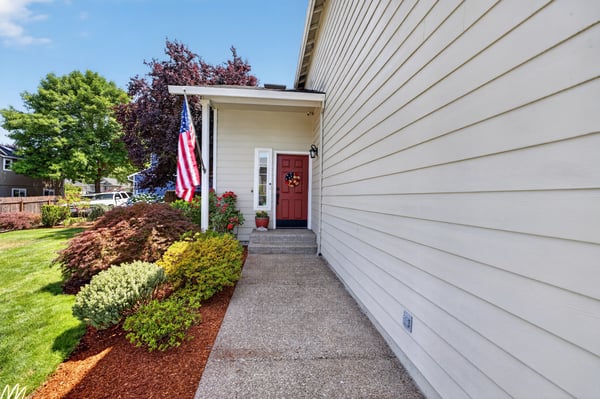 Inviting entryway features vibrant landscaping and a welcoming front porch with a bold red door.