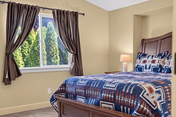 Cozy bedroom featuring a patterned quilt, natural light, and lush outdoor views from the window.