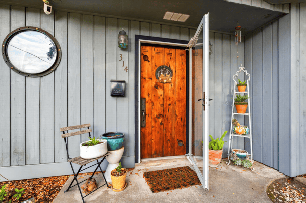 Inviting entryway featuring a striking wood door, potted plants, and a cozy seating area.