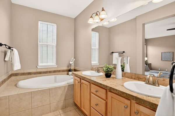 Spacious bathroom featuring dual sinks, a relaxing tub, and natural light from large windows.