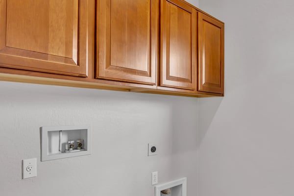 Functional laundry room with overhead cabinets and durable tile flooring, adding convenience and storage space.