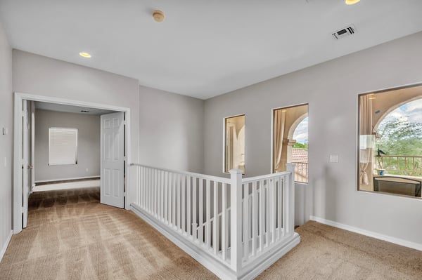 Versatile upper-level landing with open railing and bright windows, ideal as a transition space or reading nook.