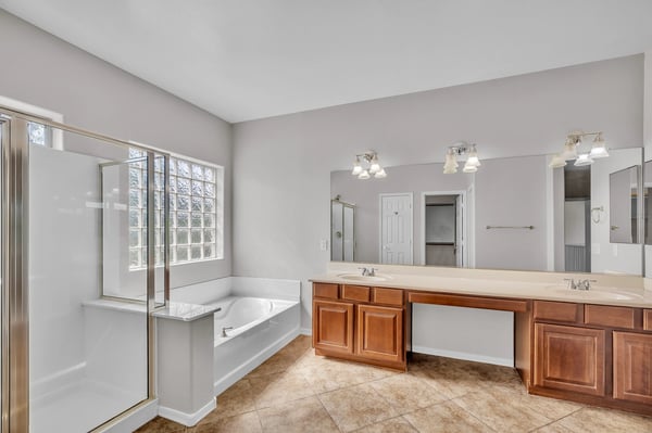 Elegant primary bathroom with soaking tub, dual sinks, and separate shower, complemented by natural light and spacious design.