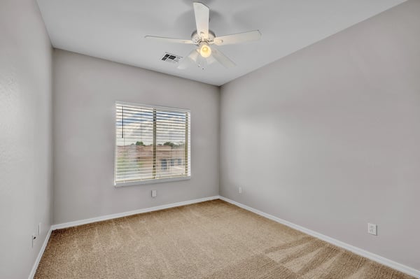 Comfortable bedroom with plush carpet, ceiling fan, and natural light, ideal for guests or a home office setup in Goodyear.