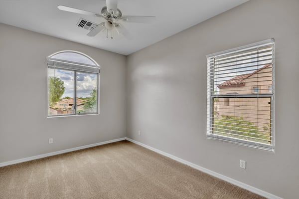 Bedroom with dual windows bringing in natural light and outdoor views, complemented by carpet flooring and ceiling fan in Goodyear.