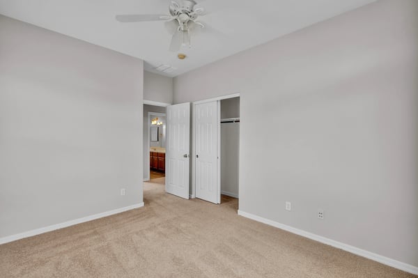 Convenient bedroom located near a bathroom, featuring neutral tones, plush carpet, and ceiling fan for comfortable living in Goodyear.
