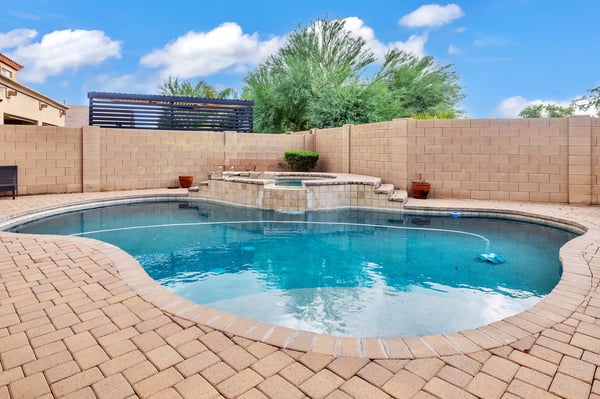 Stylish pool with raised spa and water feature, complemented by paver decking and privacy walls for a serene backyard setting in Goodyear.