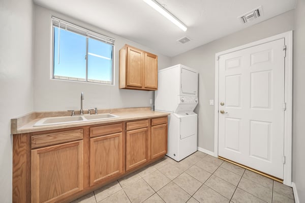 Dedicated laundry room featuring built-in cabinets, a utility sink, and included stacked washer and dryer. Functional design makes daily chores simple while providing excellent storage.
