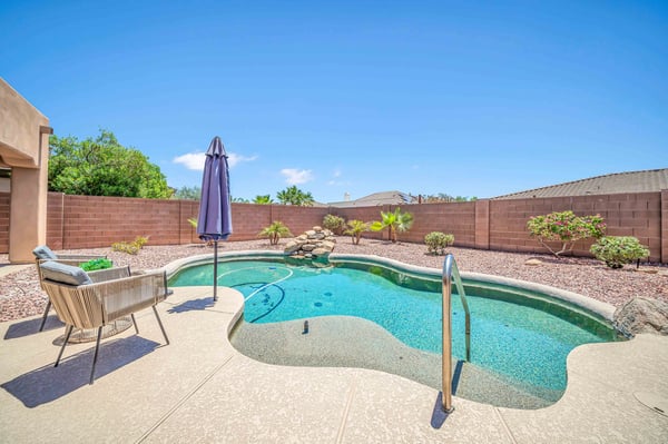 Beautiful backyard with a sparkling PebbleTec pool, waterfall feature, and spacious patio surrounded by mature desert landscaping. Designed for relaxing afternoons and memorable gatherings.