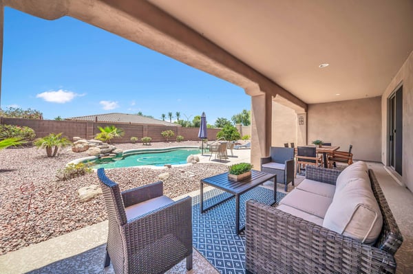 Covered patio with comfortable seating and dining space overlooks the private backyard and PebbleTec pool, creating seamless indoor-outdoor living. A perfect extension of the home's open floor plan for entertaining or relaxing.
