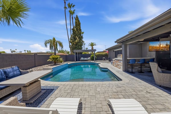 Beautiful heated pool is complemented by expansive paver decking, lounge chairs, covered bar seating, and professionally designed outdoor living spaces in this Scottsdale home.
