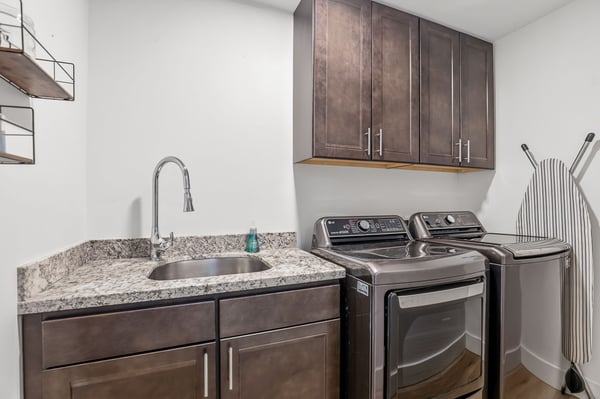 Modern laundry room features a utility sink, granite countertops, overhead cabinetry, and quality appliances, delivering convenience and additional storage for everyday living.