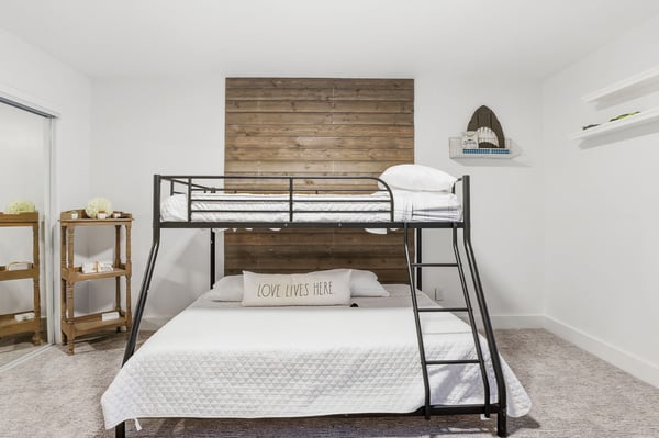 Comfortable guest bedroom features a bunk bed, custom wood accent wall, mirrored closet doors, plush carpeting, and generous space for family or overnight guests in this Scottsdale home.
